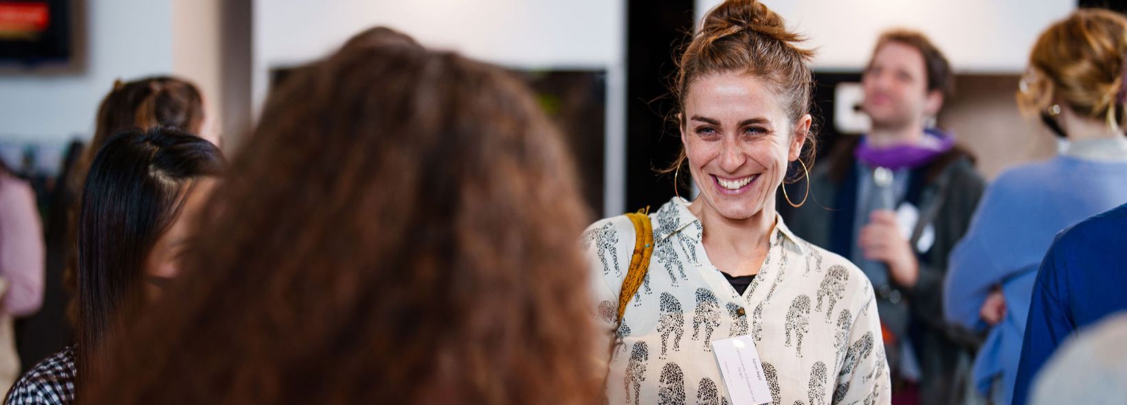 Woman smiling towards camera in discussion with another person whose back is towards the viewer