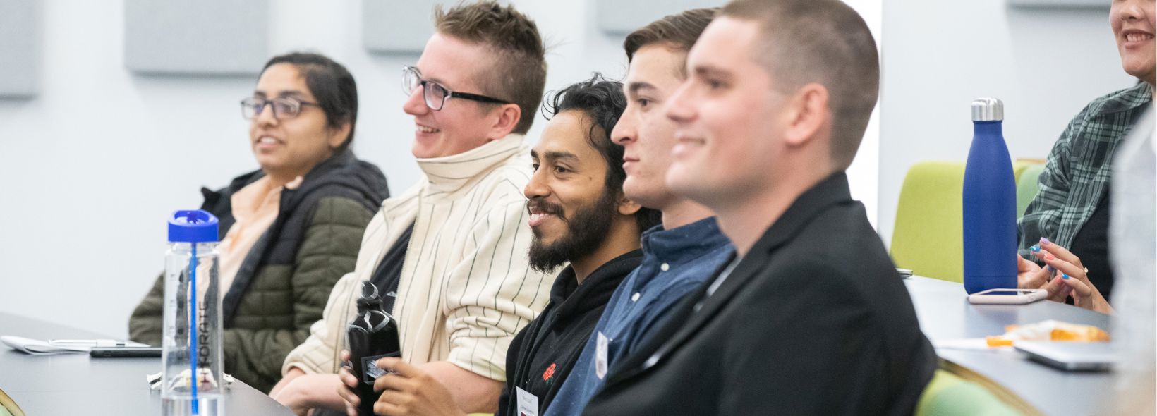 Side profiles of a group of people lined up behind a table in a lecture setting